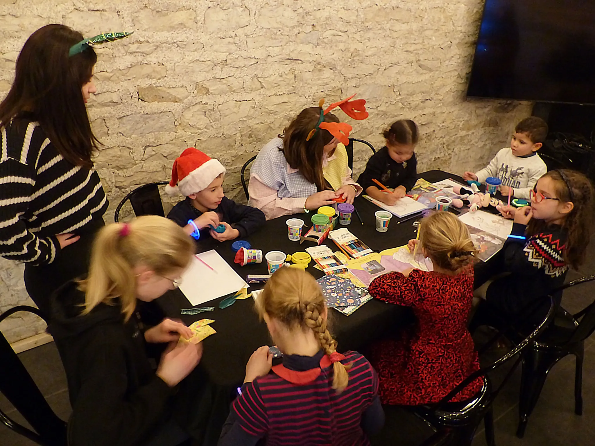 Des enfants dessinent à une table en compagnie d’une babysitter.